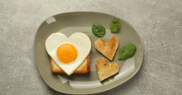 Jajko sadzone w kształcie serca na grzance, obok tostów w kształcie serc i liści szpinaku.
