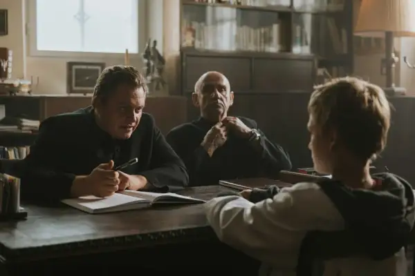 Trzech mężczyzn przy stole, jeden z nich pisze. Scena z filmów Piotra Domalewskiego.