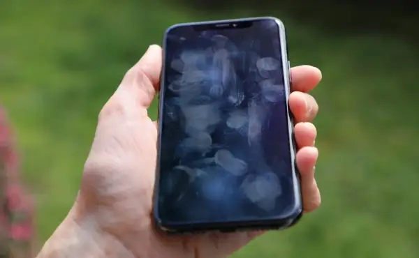 Dłoń trzyma smartfon z licznymi śladami palców na ekranie. Czy to efekt braku szkła hartowanego 9D?