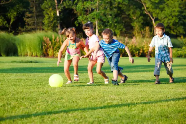 Niños jugando a la pelota en el césped, disfrutando de divertidos juegos con pelotas para niños al aire libre.
