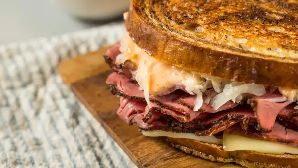 Un delicioso bocata de pastrami con pan tostado, queso fundido y chucrut.