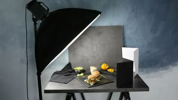 A food photography setup with burgers, salad, and a yellow pepper, illuminated by a large softbox, showcasing effective diy photography lighting.