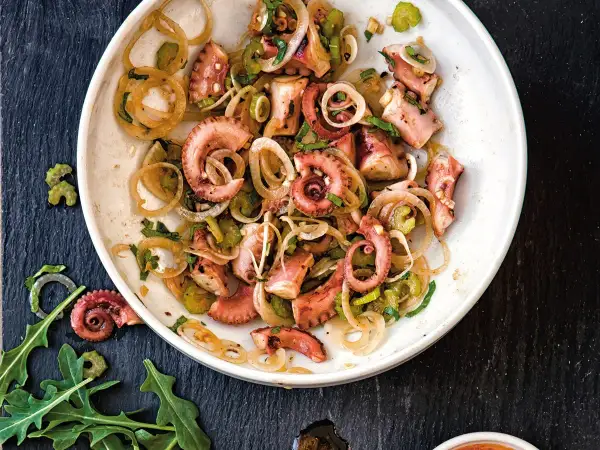 Un delicioso salpicón de pulpo con cebolla y perejil, servido en un plato blanco sobre una pizarra oscura.