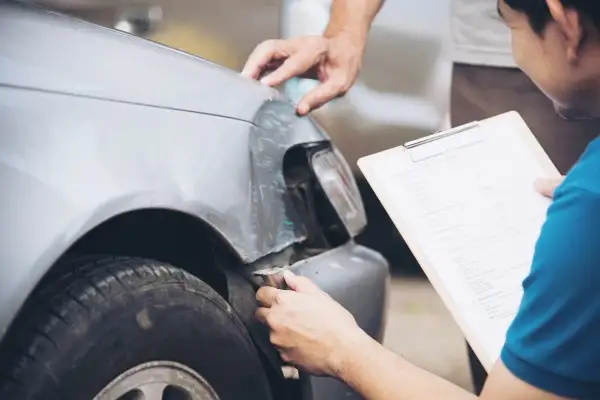 Deux hommes examinent les dégâts sur une voiture, peut-être suite à un délit de fuite. L'un tient un formulaire de déclaration de sinistre.