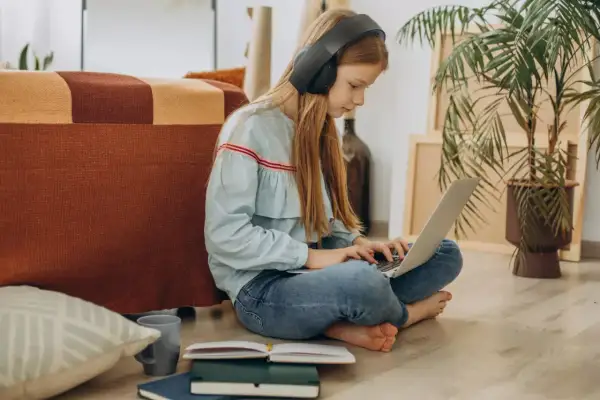 Dziewczynka w słuchawkach uczy się na laptopie, przygotowując argumenty, jak przekonać rodziców do szkoły w chmurze.