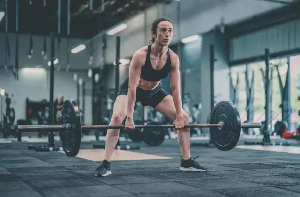 Femme concentrée en position pour un soulevé de terre, haltères lourds prêts à être soulevés dans une salle de sport.