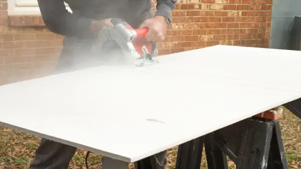 A person demonstrates how to cut cement board with a circular saw, creating a cloud of dust.