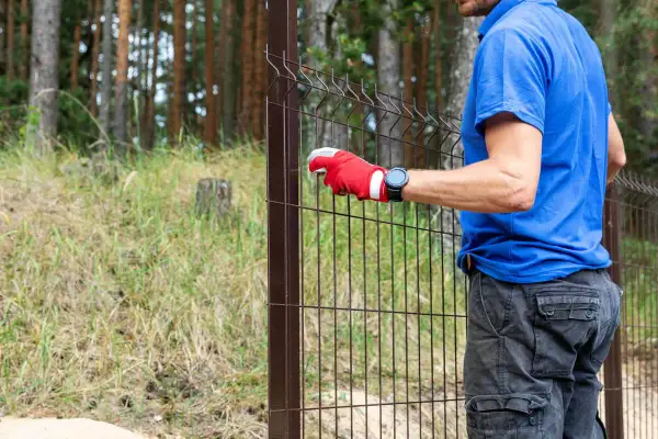 Pracownik w czerwonej rękawicy montuje ogrodzenie. Sprawdź wykonanie ogrodzenia ceny robocizny.