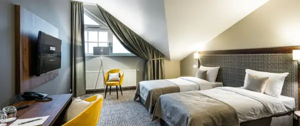 Pokój hotelowy z dwoma łóżkami, żółtym fotelem i biurkiem. Idealne miejsce na nocleg, gdzie gwiazdki w hotelach są gwarancją komfortu.
