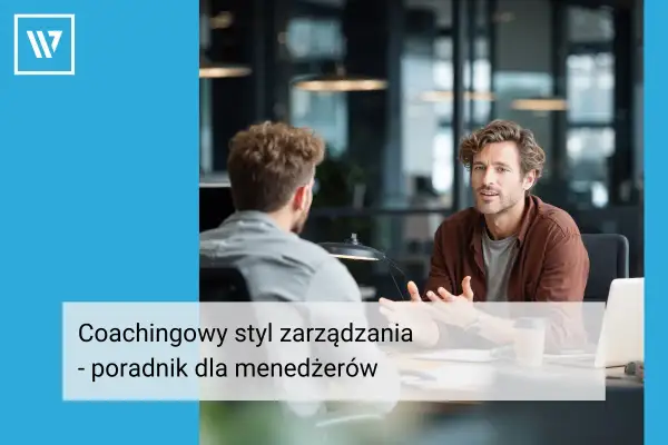 Dwóch mężczyzn rozmawia przy biurku. Jeden z nich, w brązowej koszuli, gestykuluje, wyjaśniając coś. Widać, że stosuje coachingowy styl zarządzania, wspierając pracownika.