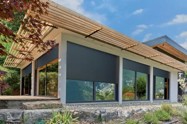 Volets roulants gris anthracite sur une maison moderne avec pergola en bois. La **couleur volet bois** des lames de la pergola contraste avec le gris des volets.