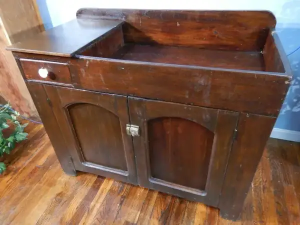 A vintage wooden dry sink with a drawer and cabinet doors, perfect for a rustic kitchen or bathroom.
