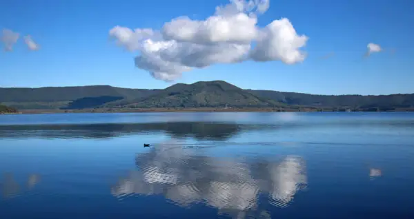 Un'oasi di pace al lago di Vici, con un cielo azzurro punteggiato da nuvole bianche che si specchiano sull'acqua calma.