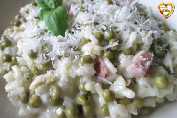 Creamy risotto with peas, ham, and grated cheese, garnished with a basil leaf.
