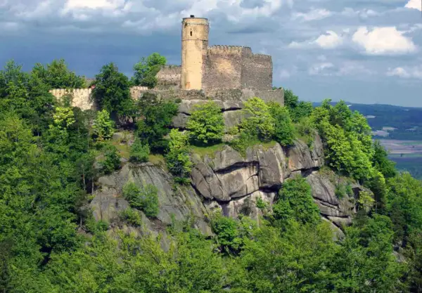 Zamek Chojnik góruje nad skalistym zboczem, otoczony bujną zielenią drzew.