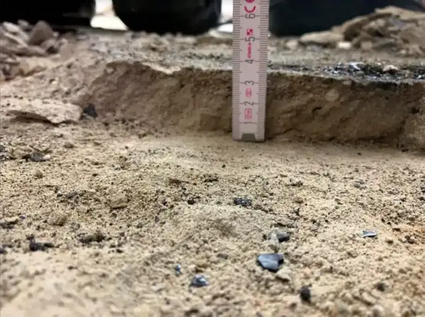 Mesure de la profondeur du décaissement du sol avec une règle. Le sable et les débris sont visibles.