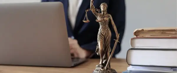 Justitia-Statue neben Laptop und Büchern. Ein Anwalt prüft Unterlagen, vielleicht wegen eines Widerspruchs Pflegegrad.