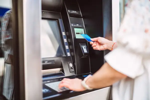 Kobieta wkłada kartę do bankomatu, przygotowując się, jak wziąć debet. Wpisuje PIN na klawiaturze.