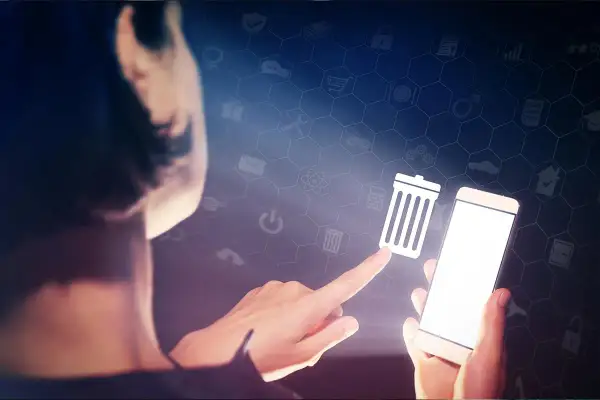 Dłoń dotyka ikony kosza na śmieci na ekranie smartfona, symbolizując czyszczenie telefonu i porządkowanie danych.