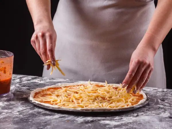 Ręce posypują pizzę startym serem. Zastanawiasz się, jaki ser do pizzy będzie najlepszy? Ten wygląda apetycznie!