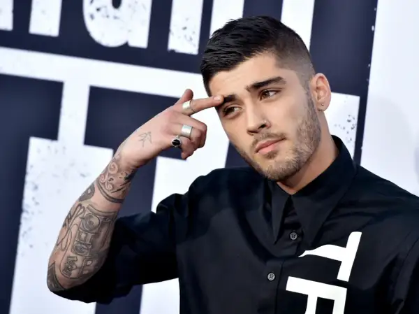 Zayn Malik, były członek One Direction, z tatuażami na ramieniu i palcami ozdobionymi pierścionkami, dotyka czoła.