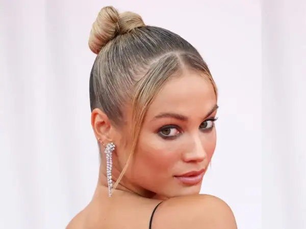Elegancka, gładka fryzura typu sleek bun z błyszczącymi kolczykami.
