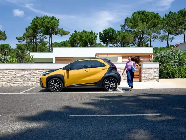 Une jeune femme se dirige vers sa voiture jaune et noire, une **voiture jeune permis automatique** parfaite pour débuter.