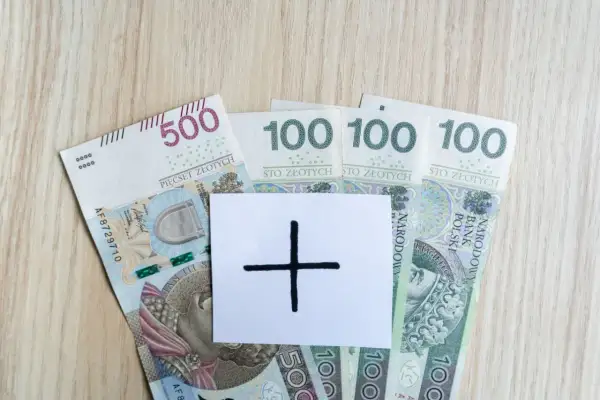 Polskie banknoty 500 i 100 zł. Na białej kartce symbol plusa, sugerujący dodatkowe środki, np. specjalny zasiłek opiekuńczy.