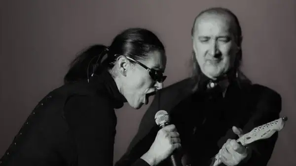 Kora śpiewa do mikrofonu, a obok niej gra na gitarze muzyk. To scena z koncertu, gdzie można usłyszeć maanam piosenki alfabetycznie.