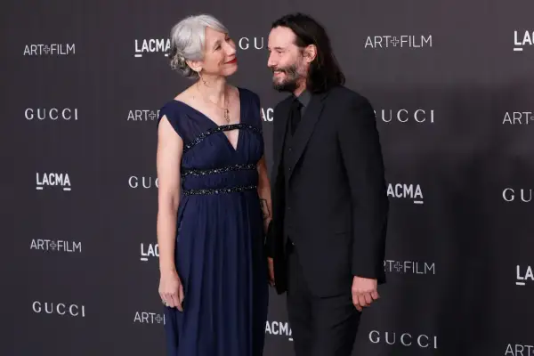 Keanu Reeves i jego żona Alexandra Grant patrzą na siebie z uśmiechem na tle logo Gucci i Art+Film.