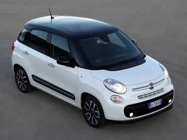 Biały Fiat 500L z czarnym dachem i felgami, zaparkowany na szarym podłożu.