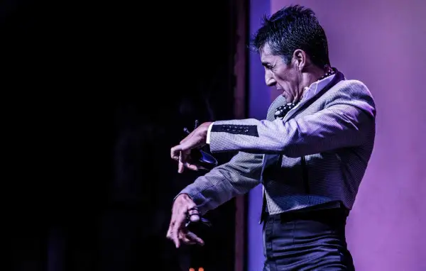 Un hombre con traje a cuadros realiza un apasionado flamenco baile, con las manos extendidas y castañuelas.