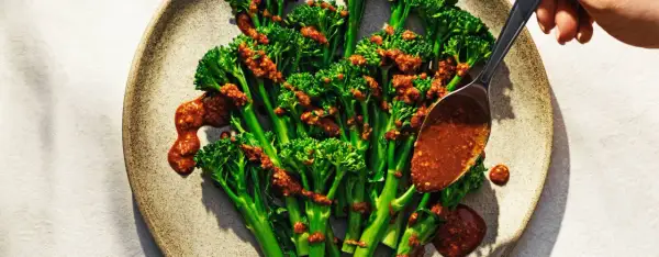 Ånga broccoli med en kryddig sås. En sked häller över mer sås på de gröna buketterna.