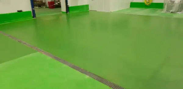 Suelo de nave industrial de color verde brillante, con un desagüe metálico en diagonal.