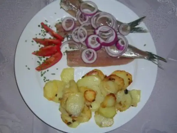 Matjes mit Bratkartoffeln, garniert mit Zwiebelringen und Tomaten. Ein klassisches Gericht, das auf einem weißen Teller serviert wird.