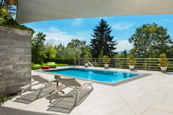 Moderne poolumrandungen ideen: ein rechteckiger Pool mit türkisfarbenem Wasser, umgeben von hellen Terrassenplatten, Liegestühlen und grünen Sitzsäcken.
