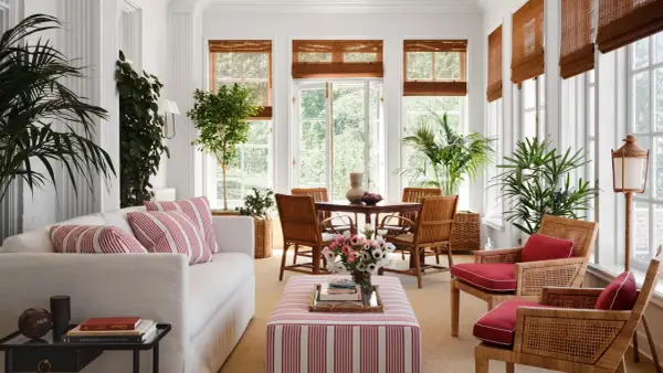 Bright sunroom with white sofa, striped ottoman, rattan chairs, and lush plants. Inspiring sunroom decorating ideas for a fresh, airy feel.
