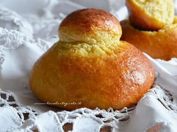 Brioches siciliane ricetta originale con strutto, dorate e soffici, su un pizzo bianco.