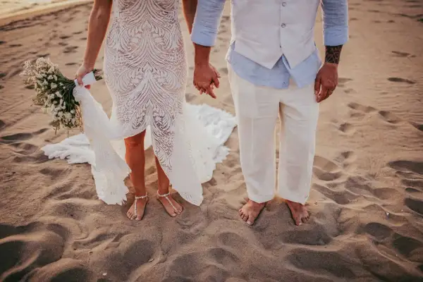 Coppia felice in un matrimonio spiaggia. La sposa con un bouquet, lo sposo con un gilet leggero.