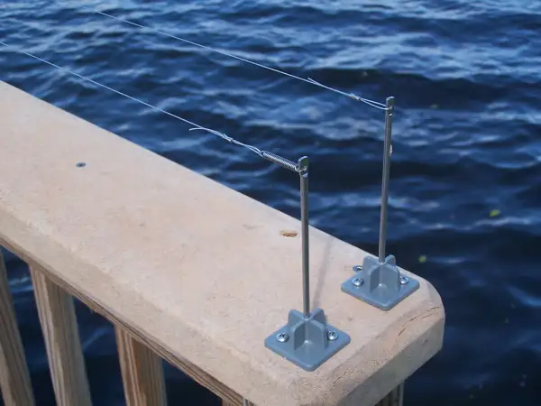 Deux piquets de pêche sur un garde-corps en bois, prêts à attraper un poisson. L'eau bleue ondule derrière.