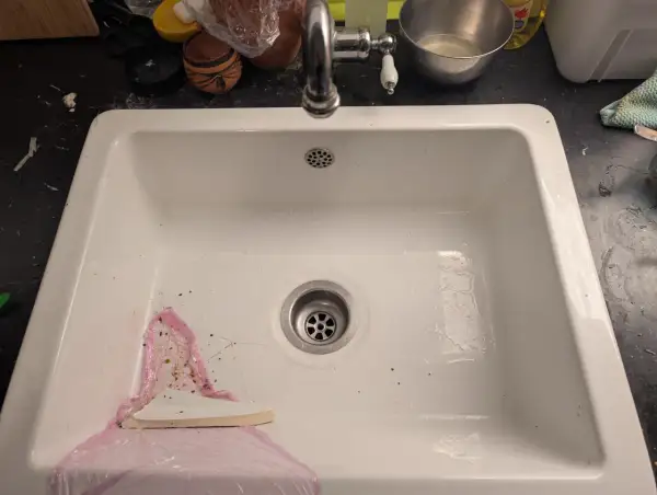 Un évier blanc avec un robinet chromé. Un outil blanc est utilisé pour aider à comment enlever un évier collé au silicone.
