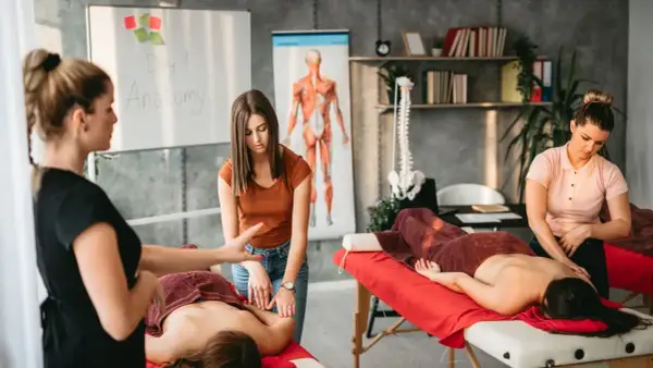 Insegnante mostra a studenti chi fa i massaggi, con diagrammi anatomici sullo sfondo.