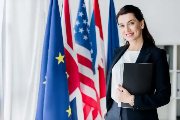 Donna sorridente con cartella, sullo sfondo bandiere UE, USA e Francia. Un futuro in scienze investigative triennale.