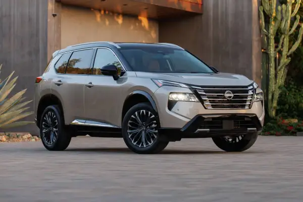Elegancki, beżowy Nissan Rogue z czarnym dachem i przyciemnianymi felgami stoi przed nowoczesnym budynkiem.