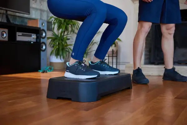 Person macht Kniebeugen auf einer Aerobic-Plattform. Die **step aerobic schuhe** sind dunkelblau mit hellblauen Akzenten.