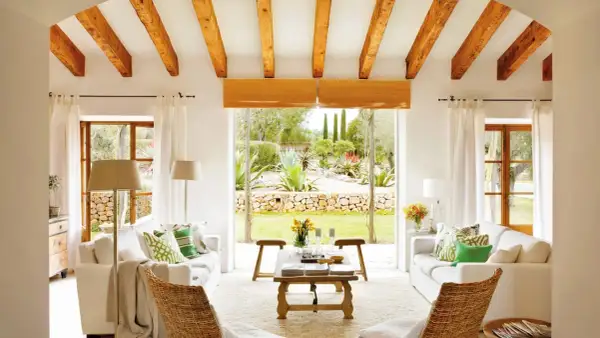 Salón con vigas de madera y vistas a un jardín exuberante, reflejo de la arquitectura mediterránea.