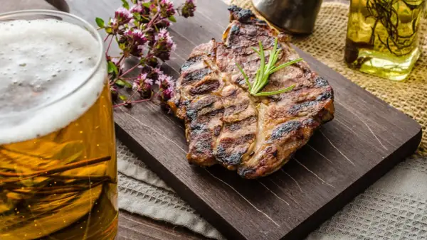 Succulenta grigliata con rosmarino, accompagnata da una birra dorata e fiori di origano.