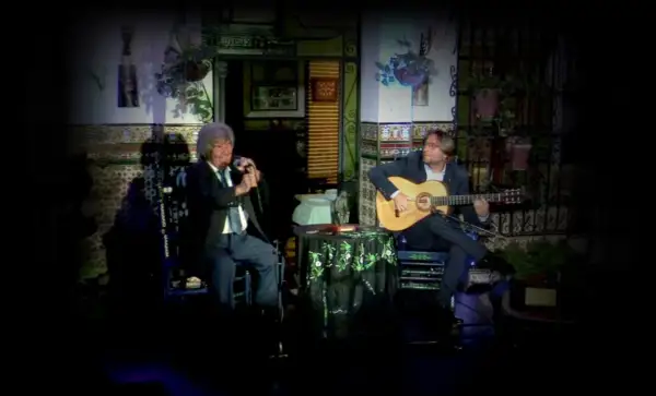 Dos hombres disfrutan de un emotivo canto flamenco. Uno canta al micrófono, el otro acompaña con su guitarra.