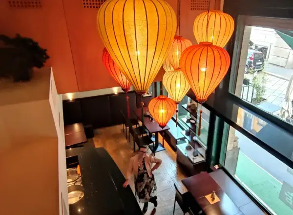 Interno di un ristorante cinese a Milano, illuminato da lanterne orientali. Una donna osserva l'ambiente.