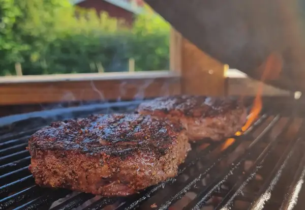 Två saftiga biffar med kryddor grillas över glödande kol. Perfekt för en sommarfest, undrar vad man kan grilla mer?